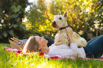 Happy mid adult caucasian lesbian woman with scottish terrier on stomach lying on blanket in yard