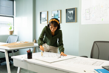 Asian young female architect drawing blueprint at table in creative office