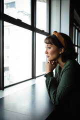 Fototapeta premium Thoughtful young asian businesswoman with hand on chin looking through window in creative office