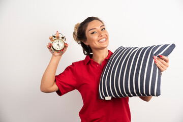 Young woman in red short showing an alarm clock and holding a pillow