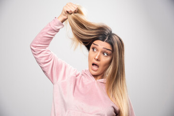 Blond lady in pink sweatshirt feels dissatisfied about her dry hair or hair color