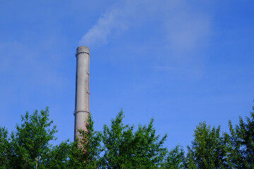 The high gray chimney of an industrial enterprise pollutes the atmosphere with emissions in the form of smoke. Industrial zone, thick clouds of smoke, exhaust gases. Climate change, ecology