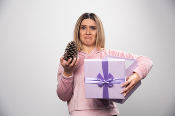 Blonde lady in pink sweatshirt takes out an oak tree cone from the gift box and feels dissatisfied