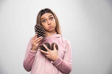 Blonde lady in pink sweatshirt makes silly positive faces with oak tree cones in the hand