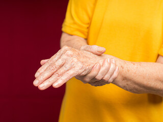 Senior woman suffering from wrist pain while standing against a red background