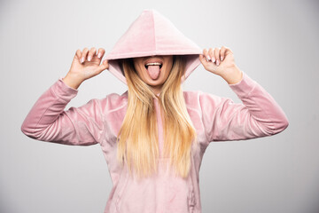 Blonde lady in pink sweatshirt making joyful and positive poses by wearing hoodie to her head
