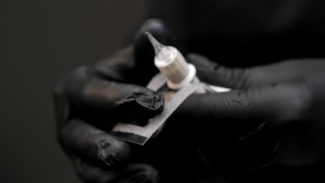 Hands in black latex gloves unpack the nozzle with a permanent makeup needle. Close-up