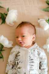 Cute baby in flower printed clothes laying in peonies