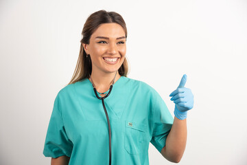 Young female nurse showing thumb up on white background