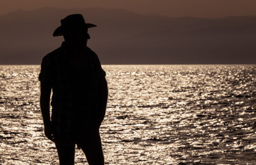 Silhouette of adult man in hat on beach during sunset