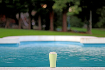 A recyclable plastic cup next to a swimming pool