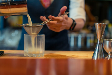 Professional male bartender preparing and serving cocktail drink to customer on bar counter at...