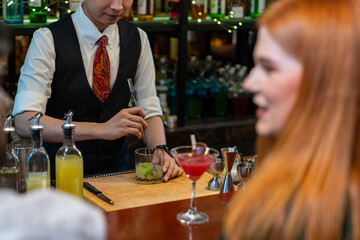 Professional male bartender preparing and serving cocktail drink to customer on bar counter at...