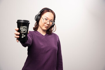 Young woman with cup posing in headphones on a white background