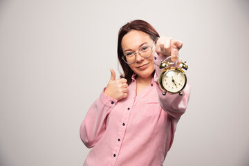 Young woman model with an alarm clock showing a thumb up on a white background