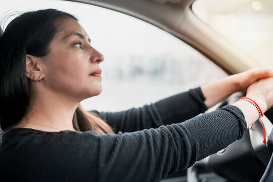 Beautiful Young Latin Woman Sitting In The Car With Her Hands On The Wheel Thoughtfully Looking At The Horizon