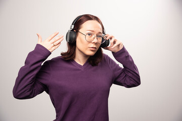 Young woman with glasses listening music in headphones on a white background