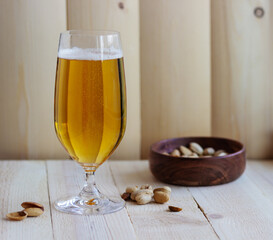 A glass of the light beer on the wooden background with a cup of pistachios