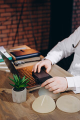 A middle-aged family doctor with a beard works in a clinic. Successful senior doctor in a white lab coat writes data to a laptop. Close-up of hands.