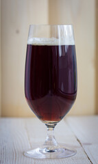 Close up of a beer glass filled with a dark craft ale, on a wood table