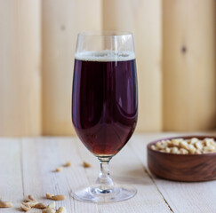 A glass of the dark beer on the wooden background with a cup of pistachios