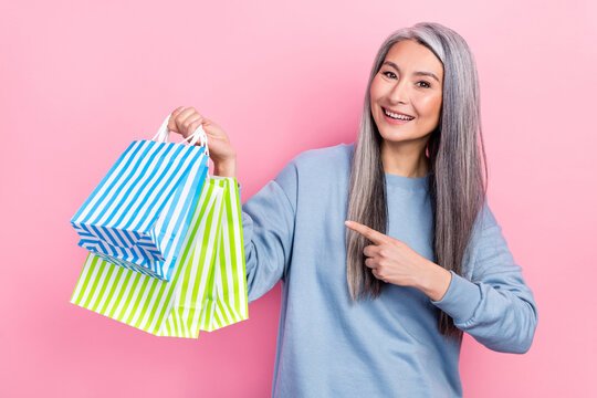Photo of dreamy sweet lady pensioner dressed blue pullover pointing finger shoppers isolated pink color background