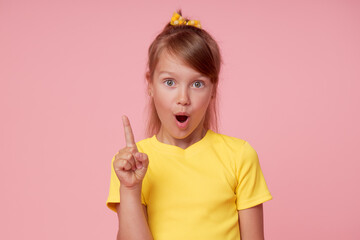 Portrait of surprised cute little toddler girl child over pink background. Looking at camera. Pointing up. Advertising childrens products.