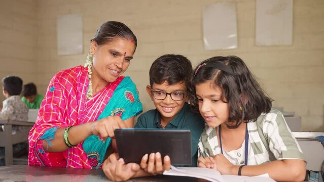 friendly Teacher explaining concepts to students from digital tablet while sitting with students on desk - concept of personal care support, assistance technology.and 