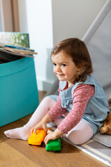 childhood, hygge and people concept - little baby girl playing with toy cars in kid's tent or...