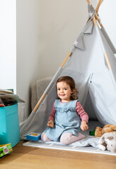 childhood, hygge and people concept - happy little baby girl playing in kid's tent or teepee at home © Syda Productions