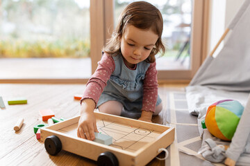 childhood, hygge and people concept - little baby girl playing with toy blocks at home