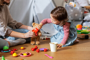 family, leisure and people concept - happy mother and little baby daughter playing tea party with set of toy dishes at home