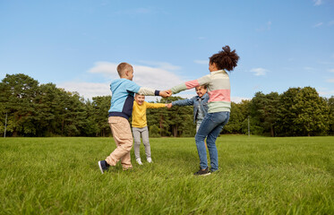 Fototapeta premium childhood, leisure and people concept - group of happy kids playing round dance at park