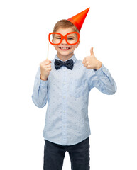 birthday, childhood and people concept - portrait of little boy in party hat with glasses showing thumbs up over white background