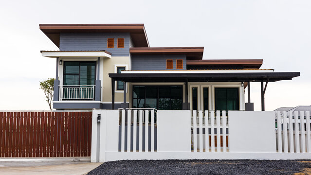 Low front view of a beautiful modern house with white concrete fence wall and brown entrance door.