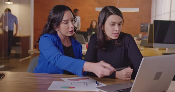 Senior business female executive looking at graphs and results with younger female staff at office workplace. Business woman coaching employee