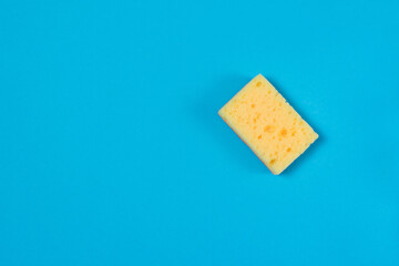 Yellow porous sponge for cleaning and washing dishes on a blue background with copy space. Homework concept.