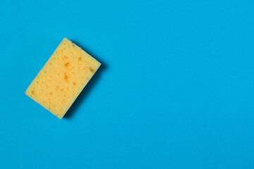 Yellow porous sponge for cleaning and washing dishes on a blue background with copy space. Homework concept.