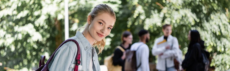 Cheerful student with backpack looking at camera in summer park, banner.