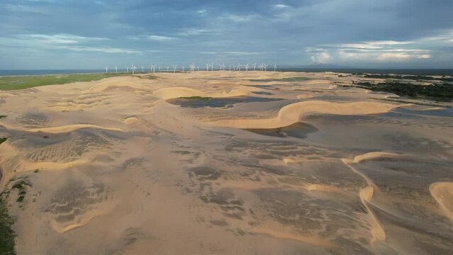 Beautiful drone take of dunes in northeast brazil at dusk, magic light and wind turbines in the background