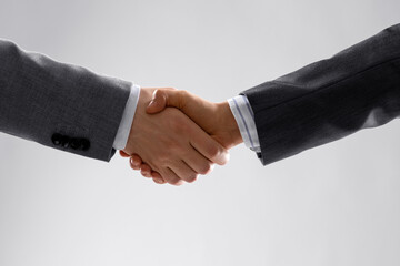 business, gesture and partnership concept - handshake of two businessmen over grey background