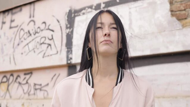 A young beautiful Caucasian woman looks into distance in thought - closeup - a wall with graffiti in the background