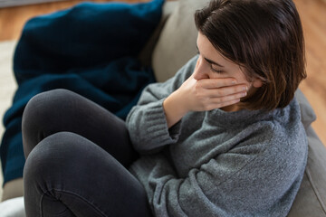 mental health, psychological problem and depression concept - stressed woman sitting on sofa at home