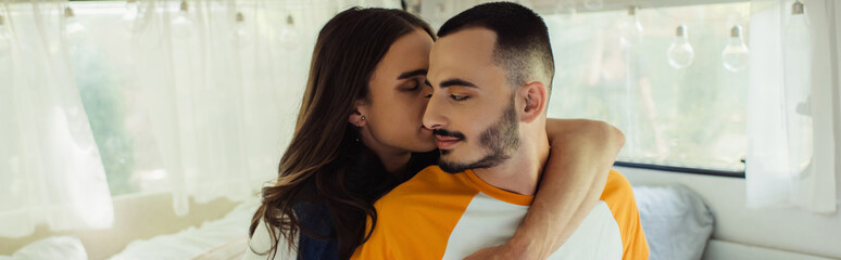 gay man with long hair and closed eyes hugging bearded boyfriend in van, banner.