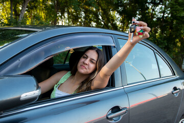 Happy teen girl driver brag receiving driving license and showing car key to the camera feeling...