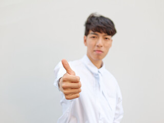 Portrait of Chinese young man with black hair in white shirt posing against white background, two thumbs up positive emotion, front view, focused on hand, blurry face.