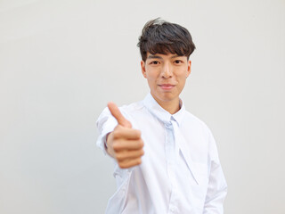 Portrait of Chinese young man with black hair in white shirt posing against white background, two thumbs up positive emotion, front view, focused on face.