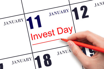 Hand drawing red line and writing the text Invest Day on calendar date January 11. Business and financial concept.