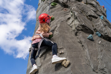 Kid in helmet having fun at bouldering wall. Little girl at outdoor climbing wall. Sports healthy...