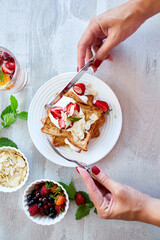 Woman hand eating breakfast of french toast with strawberries and maple syrup, good morning..